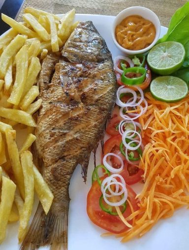 Gegrilde vis geserveerd met frietjes, groenten, limoen en dipsaus.